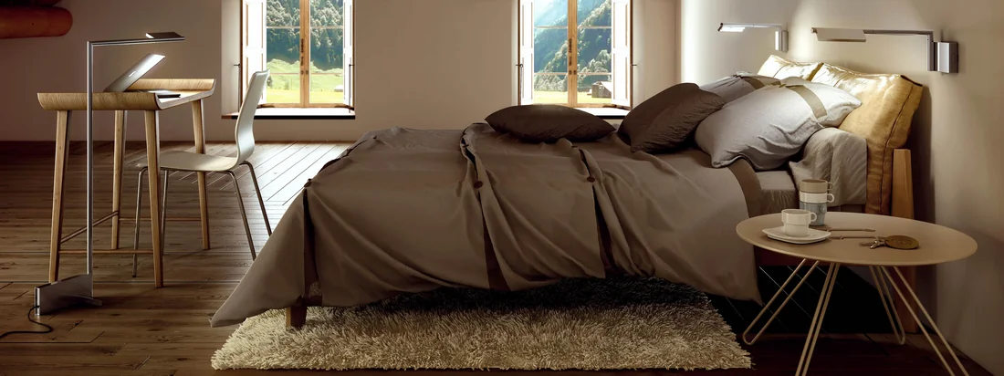 Von der Basis der Kant Leseleuchte von Estiluz geht ein Schwenkarm ab, an dem ein verstellbarer Lampenschirm befestigt ist. Die Leseleuchte eignet sich gut über dem Bett.