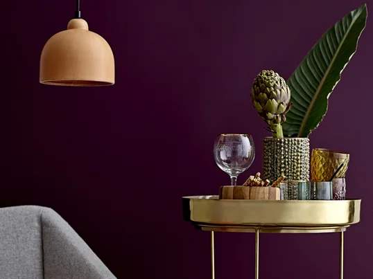 Die Noppenvase von Bloomingville in der Ambienteansicht auf einem Beistelltisch neben dem Sofa. In der Vase machen sich einzelne Blätter und eine Artischocke toll.