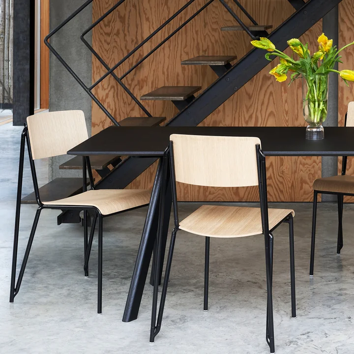 Der Petit Standard Stuhl, schwarz / Eiche matt lackiert von HAY an einem schwarzen Tisch neben der Treppe