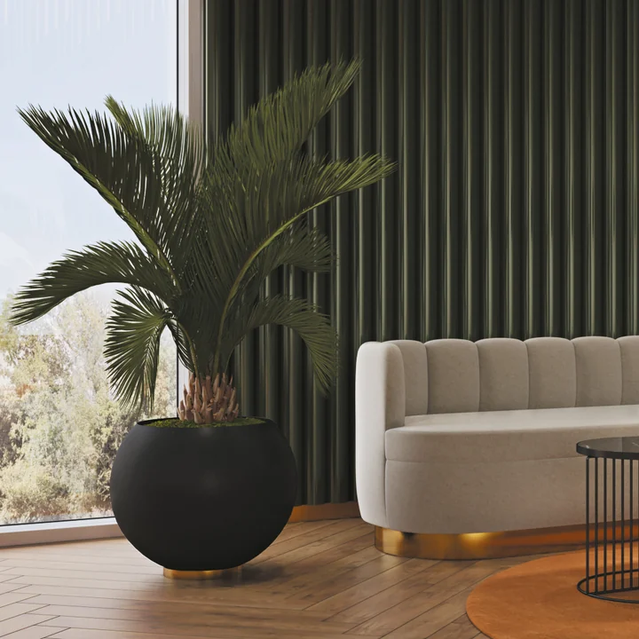 Der Globe Blumentopf von AYTM mit einer Zimmerpalme neben einer hellen Couch