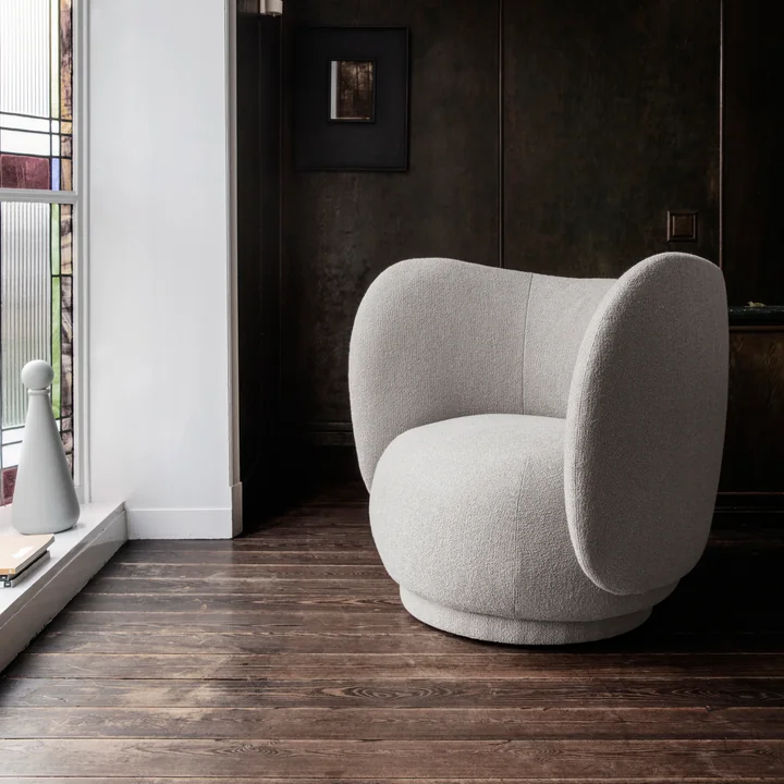 Der Rico Lounge Chair von Ferm Living auf einem dunklen Parkettboden vor einer Fensterfront
