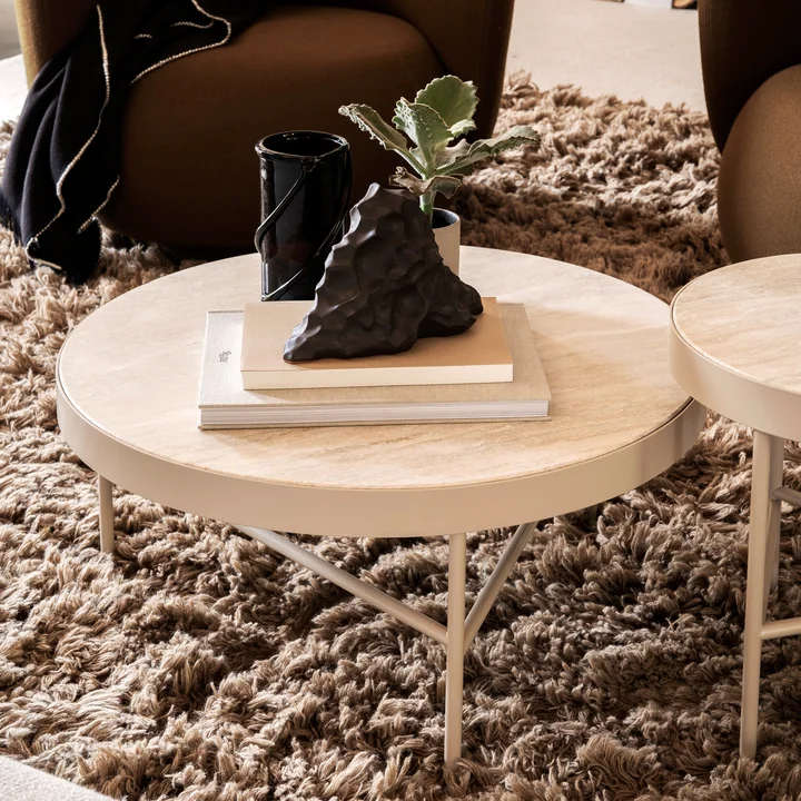 Der große Travertine Couchtisch von Ferm Living mit Büchern und Kunstobjekten auf einem flauschigen Teppich