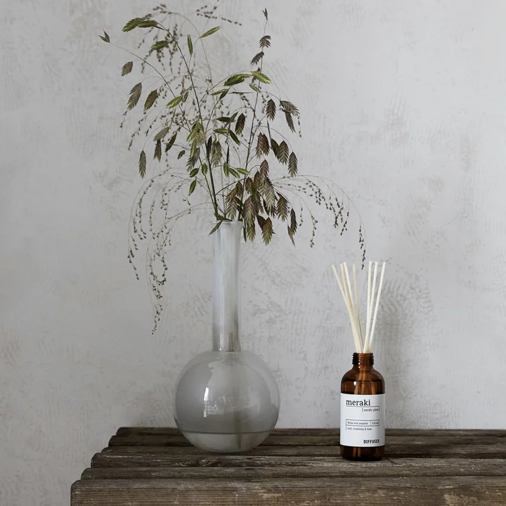 Der Raumduft mit 7 Stäbchen von Meraki auf einer Holzkommode neben einer Pflanze