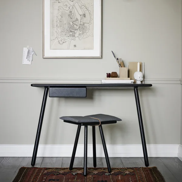 Georg Schreibtisch von Skagerak an einer grauen Wand mit schwarzem Hocker